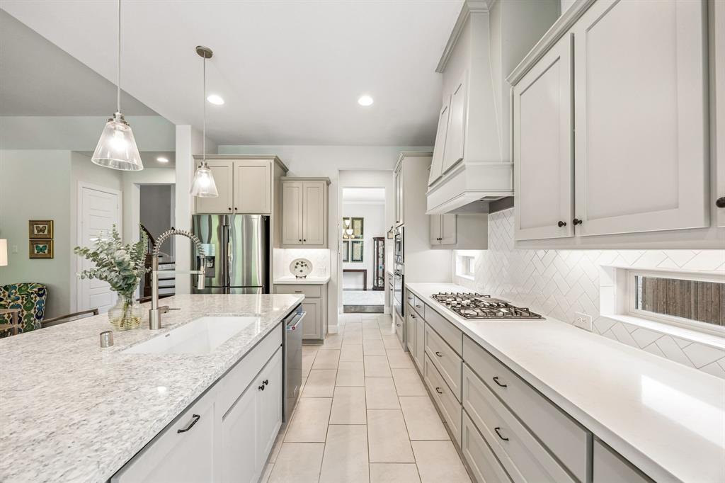 Thoughtfully designed chef's kitchen with a long, linear footprint that maximizes  counter space and storage. The heart of this kitchen features an over-sized central island with quartz countertops, a large undermount sink and pull-out trash drawer. Shaker-style cabinetry perfectly complimenting the integrated  stainless appliances and drop in gas cooktop. Large walk-in pantry between the kitchen and formal dining room seen in the background.