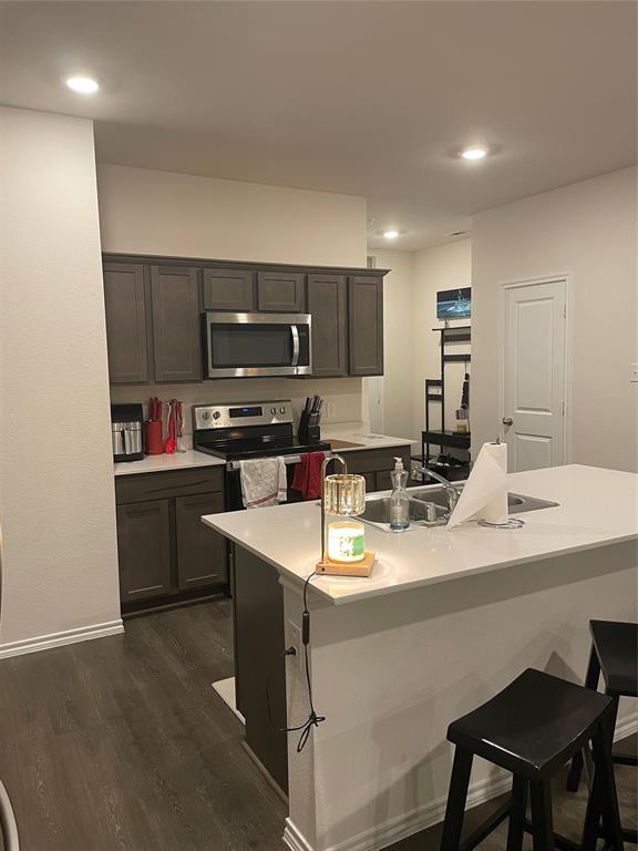 Kitchen with a breakfast bar area, stainless steel appliances, dark wood finished floors, a kitchen island with sink, and recessed lighting