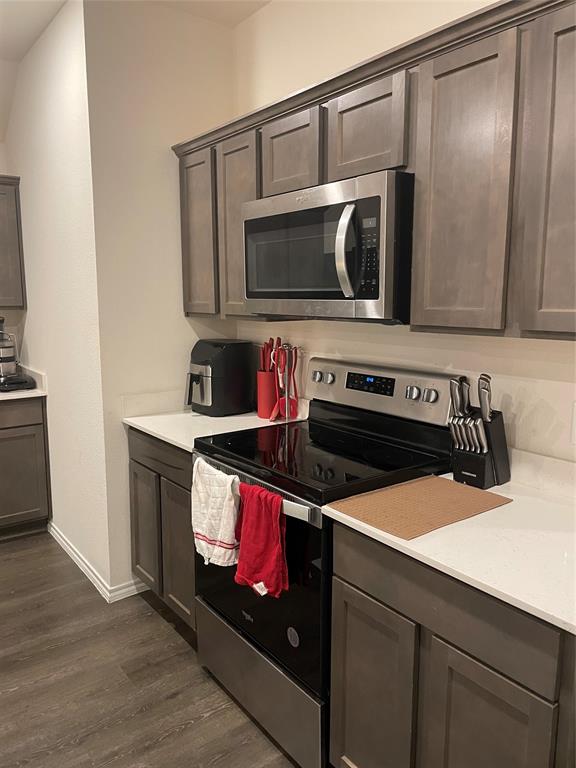Kitchen featuring stainless steel appliances, dark wood-style floors, light stone counters, and dark wood finish cabinets