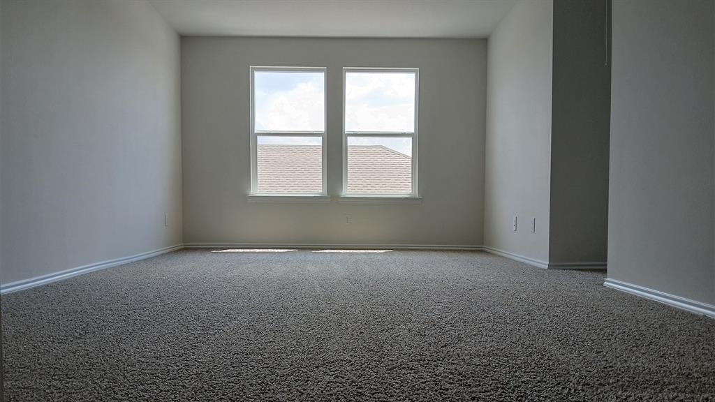 Spacious room featuring neutral carpeting, light-toned walls, and white baseboards