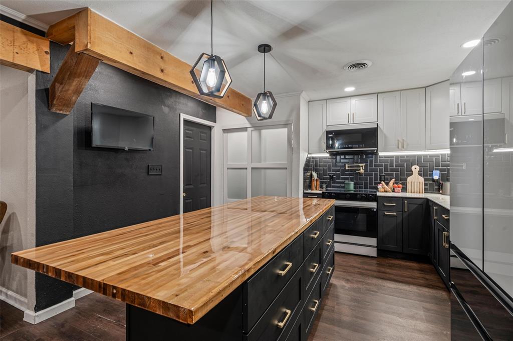 The kitchen features a spacious island with a polished wood countertop, two pendant lights, and dark wood flooring