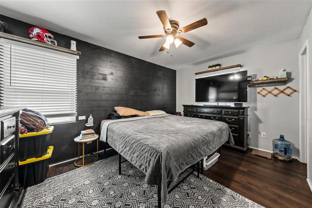 Bedroom featuring an accent wall, dark wood-style floors, ceiling fan, and wooden walls