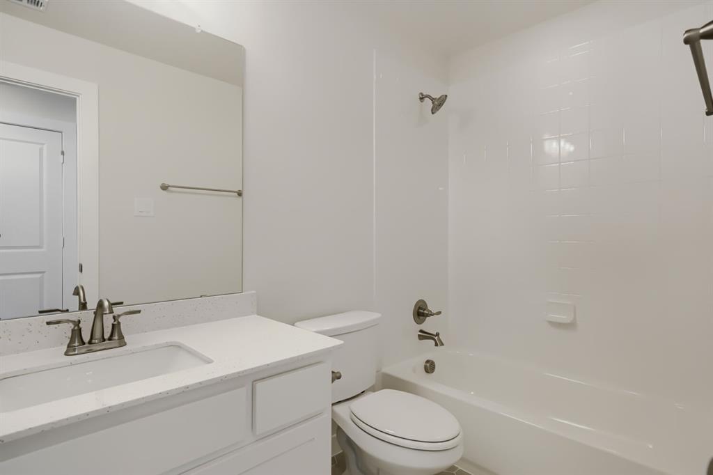 Bathroom featuring a white vanity with an integrated sink, a speckled light-toned countertop, a frameless wall mirror, and a white bathtub with a tiled surround