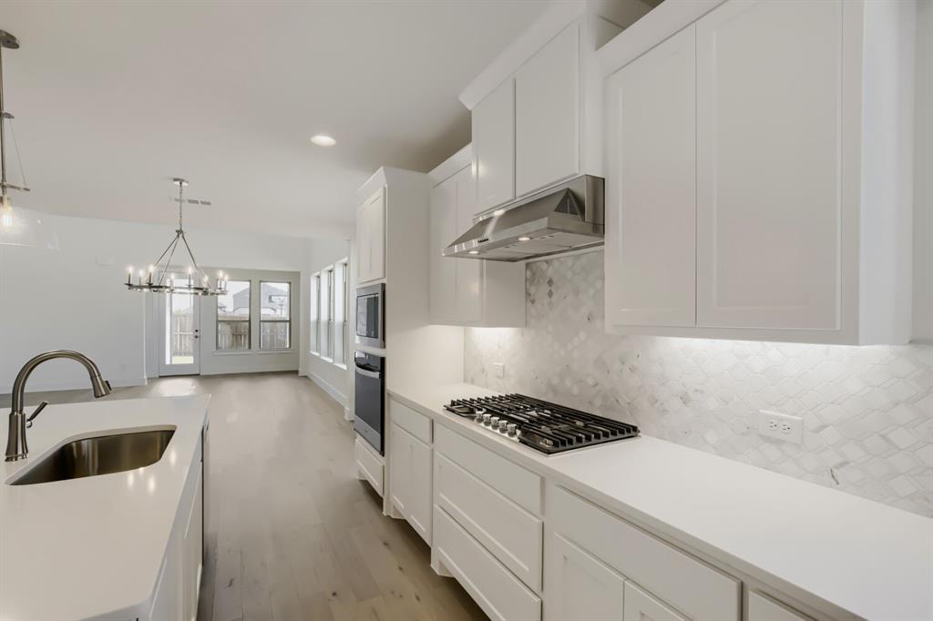 Kitchen featuring white shaker cabinetry, light-toned countertops, a stainless steel gas cooktop, built-in double ovens, and a patterned tile backsplash