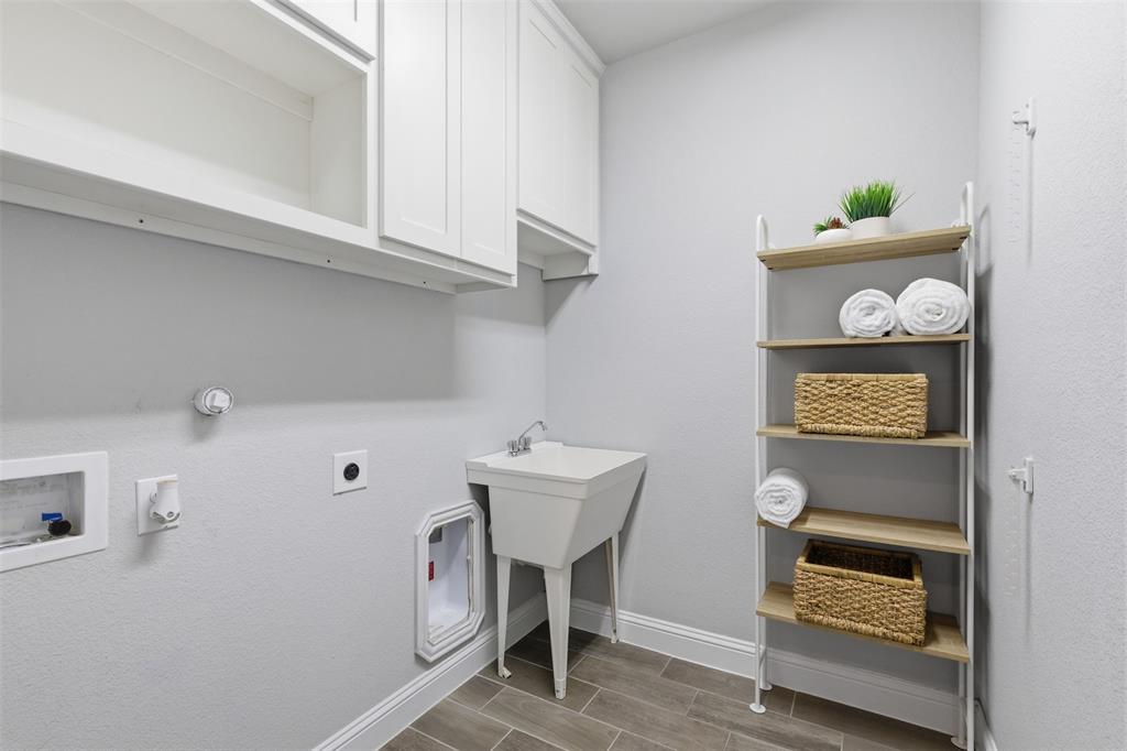 Utility room featuring wood-finish tile flooring, a built-in utility sink, and white shaker-style cabinetry with upper storage