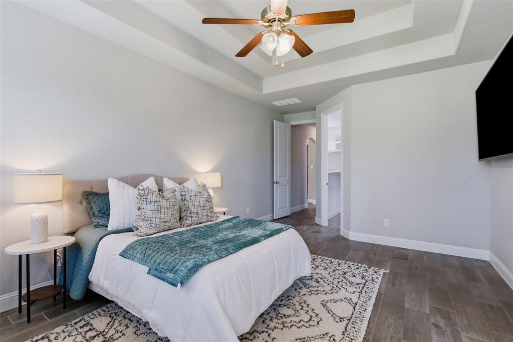 Recessed tray ceiling with a ceiling fan, wood-finish flooring, and white baseboards