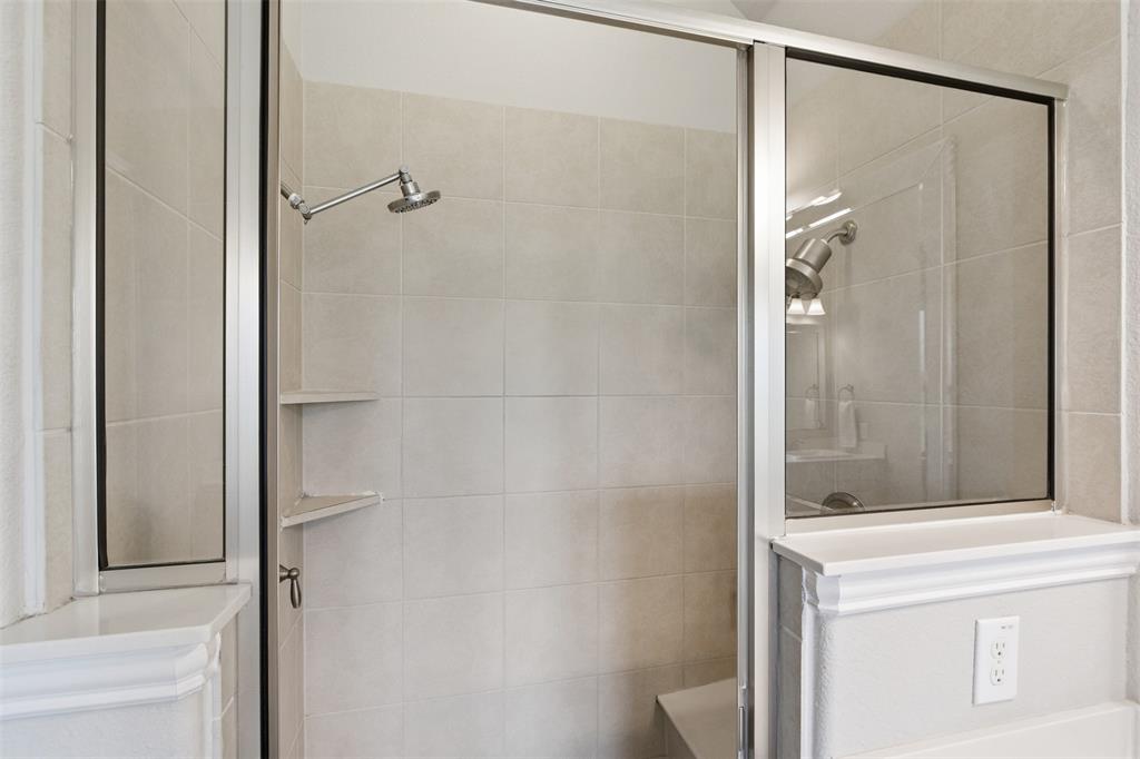 Enclosed shower with a glass sliding door, large format tile surround, built-in corner shelving, a rain shower head, and an integrated bench