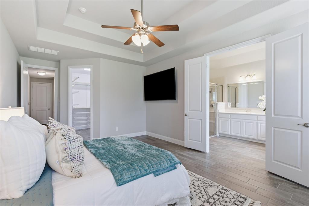 Spacious bedroom featuring tray ceilings with a ceiling fan, light gray wall paint, and wood-finish flooring