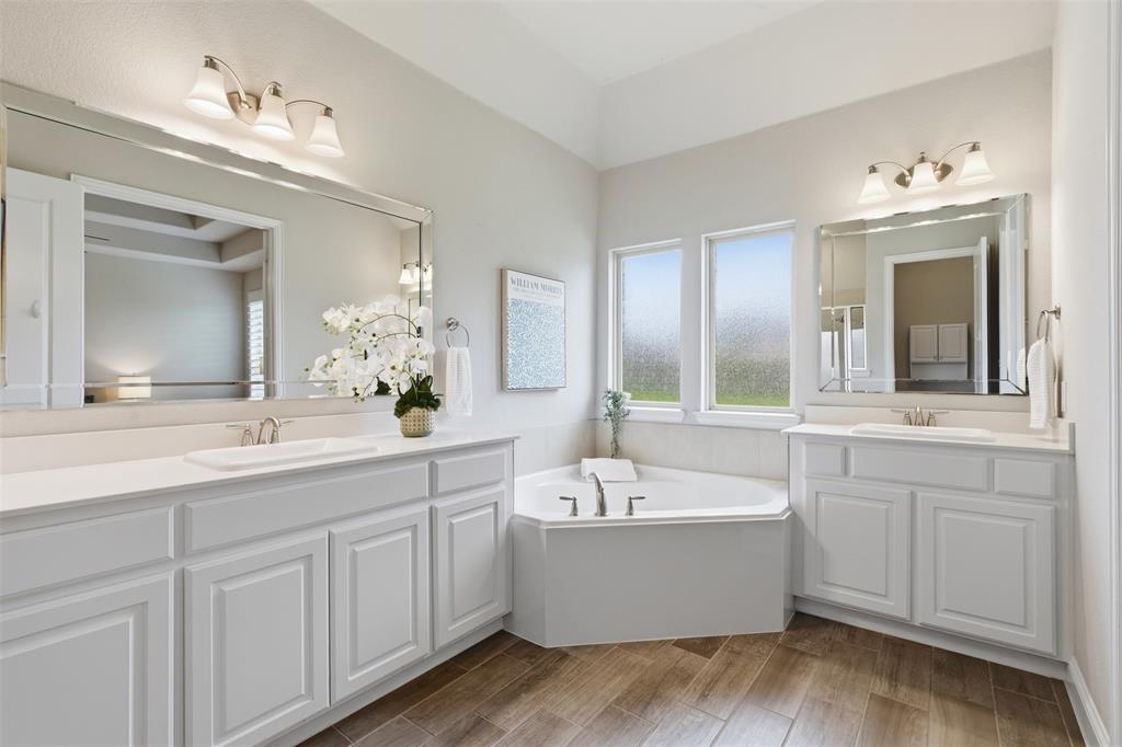Bathroom featuring a corner soaking tub, dual white vanities with undermount sinks, and wood-finish flooring
