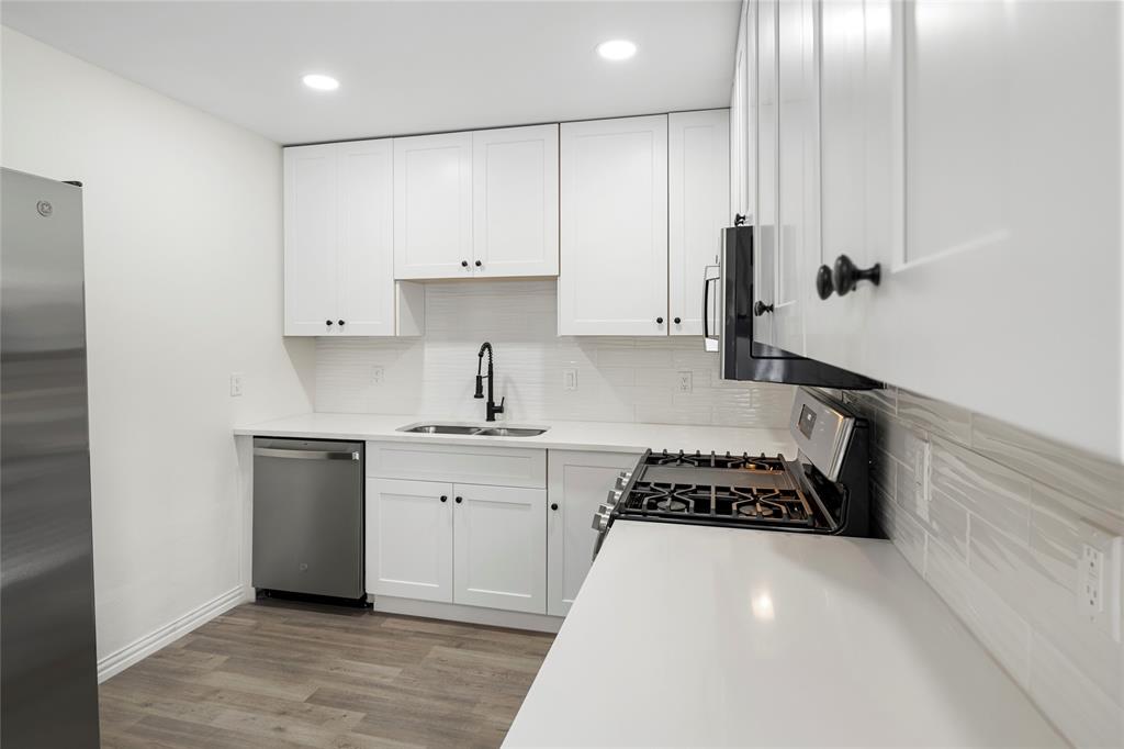 Contemporary kitchen featuring white shaker cabinetry, quartz countertops, subway tile backsplash, stainless steel appliances, and wood-finish flooring