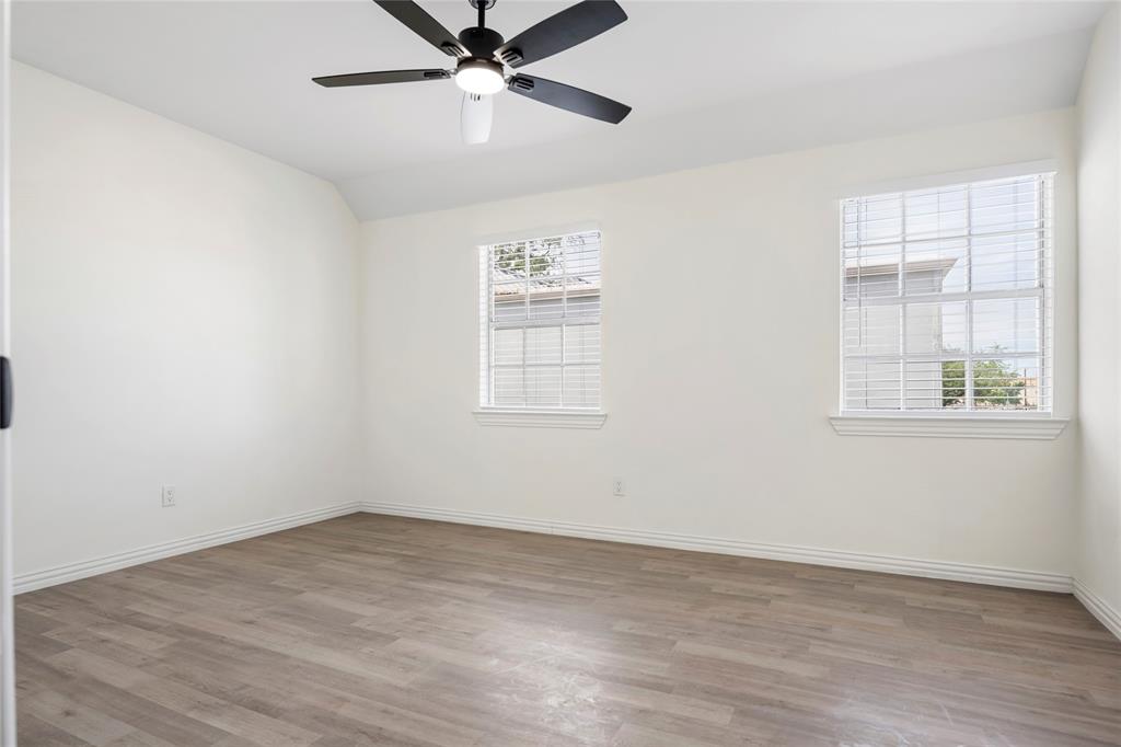 Spacious room featuring wood-finish flooring, white walls, and a ceiling fan with integrated lighting