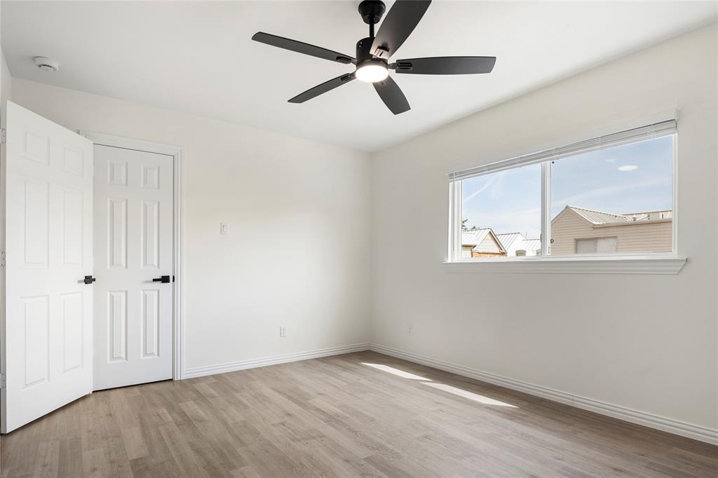 Bright room featuring a multi-pane window, wood-finish flooring, a modern black ceiling fan with integrated lighting, and white six-panel doors with matte black hardware