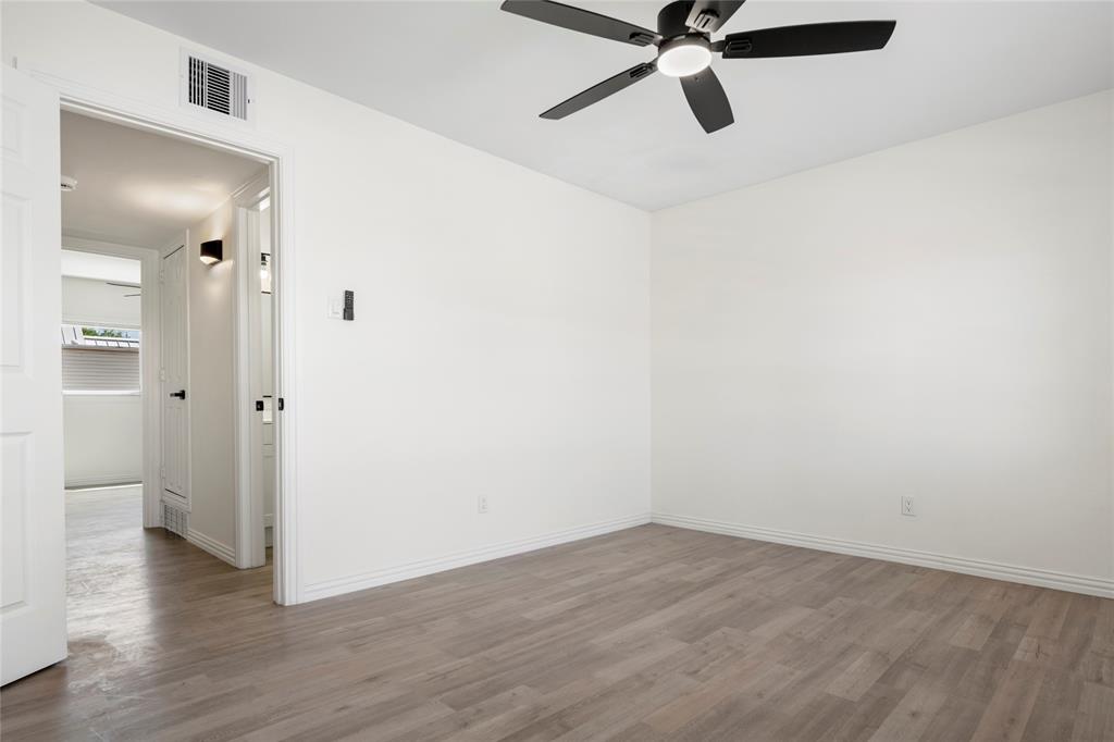 Spacious room featuring wood-finish flooring, crisp white walls, a modern ceiling fan with integrated lighting, and white baseboards