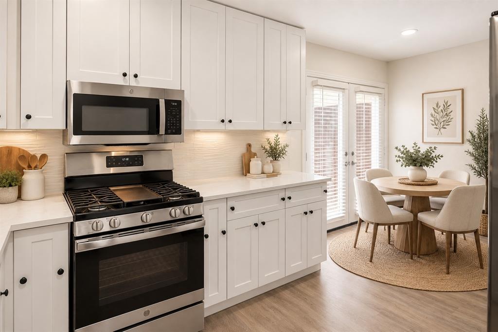 Crisp white cabinetry, stainless steel range and microwave, light-toned countertops, wood-finish flooring, and French doors