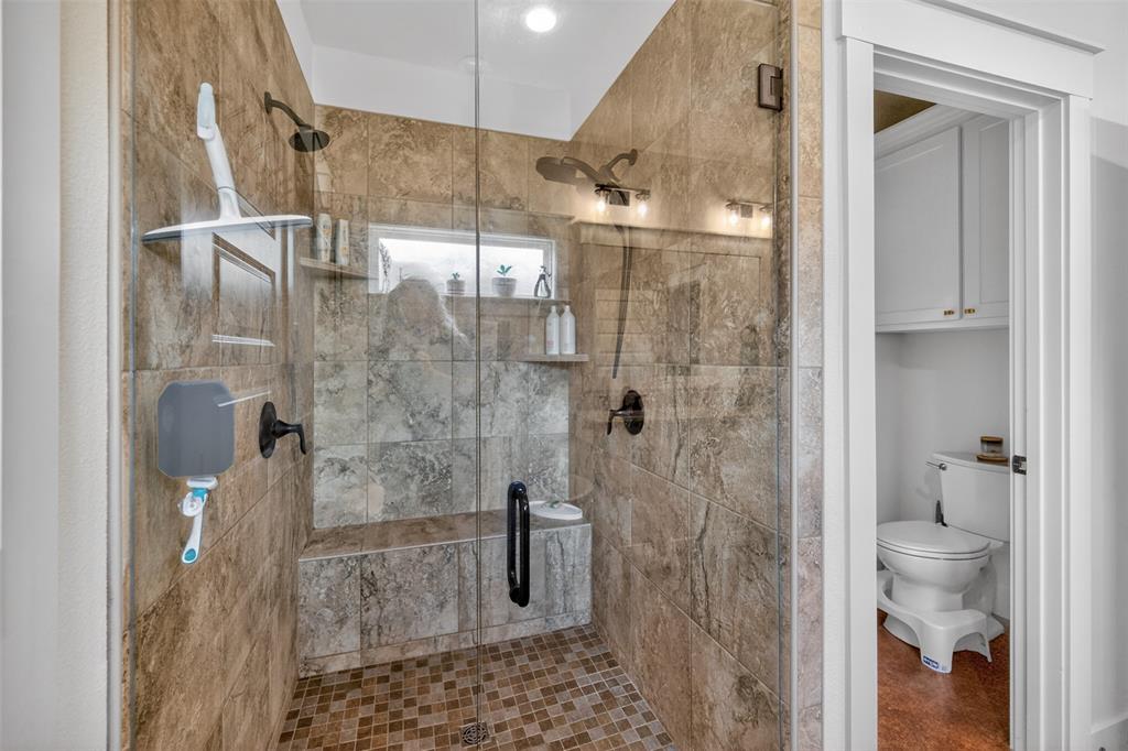 The bathroom features a spacious shower with glass enclosure, tiled walls and floor, built-in shelving, and a shower bench