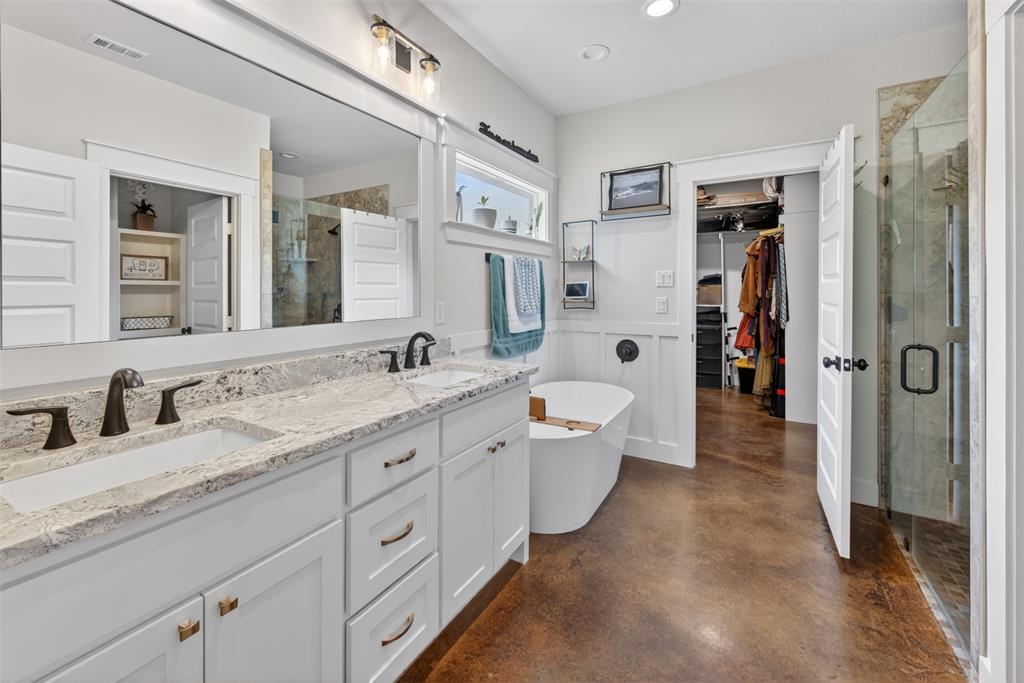 The bathroom features a double vanity with granite countertops, a freestanding bathtub, and a glass-enclosed shower