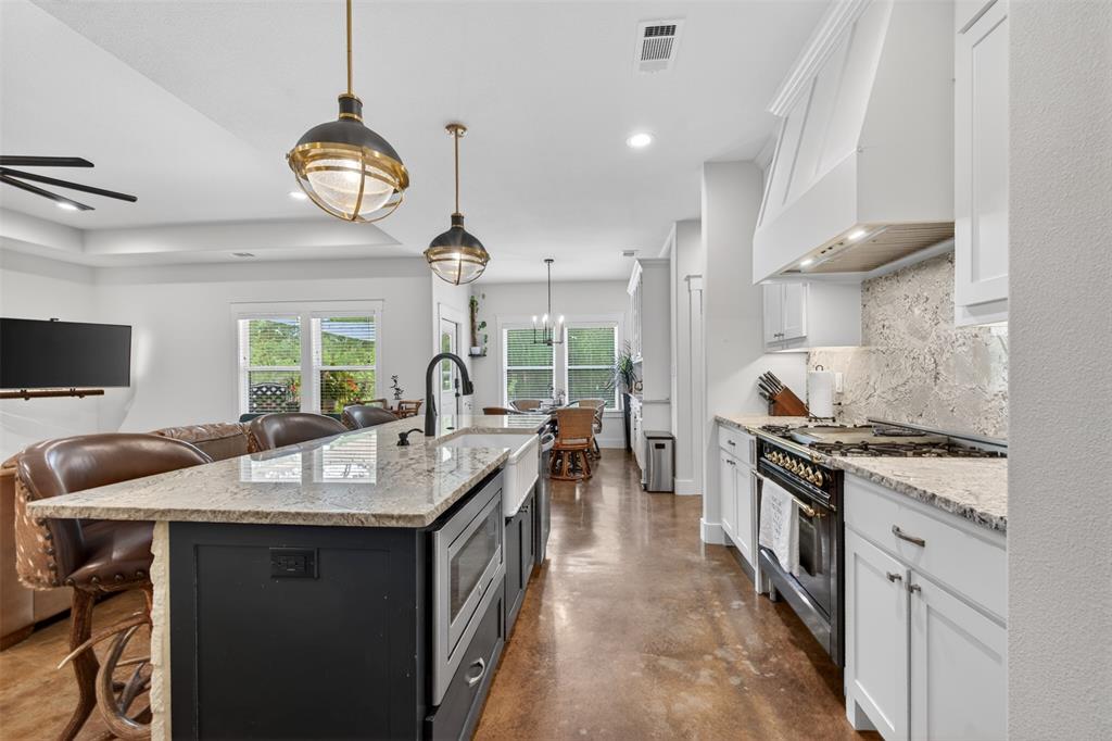 The kitchen features white cabinetry, a large kitchen island with a farmhouse sink, granite countertops, and an ILVE custom commercial range with a matching hood