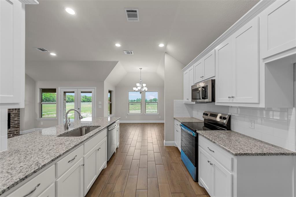Kitchen featuring a deep stainless steel sink, granite-style countertops, wood-finish flooring, white cabinetry, and stainless steel appliances