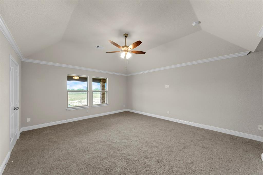 Spacious room featuring vaulted ceilings, crown molding, a ceiling fan, and carpeted flooring