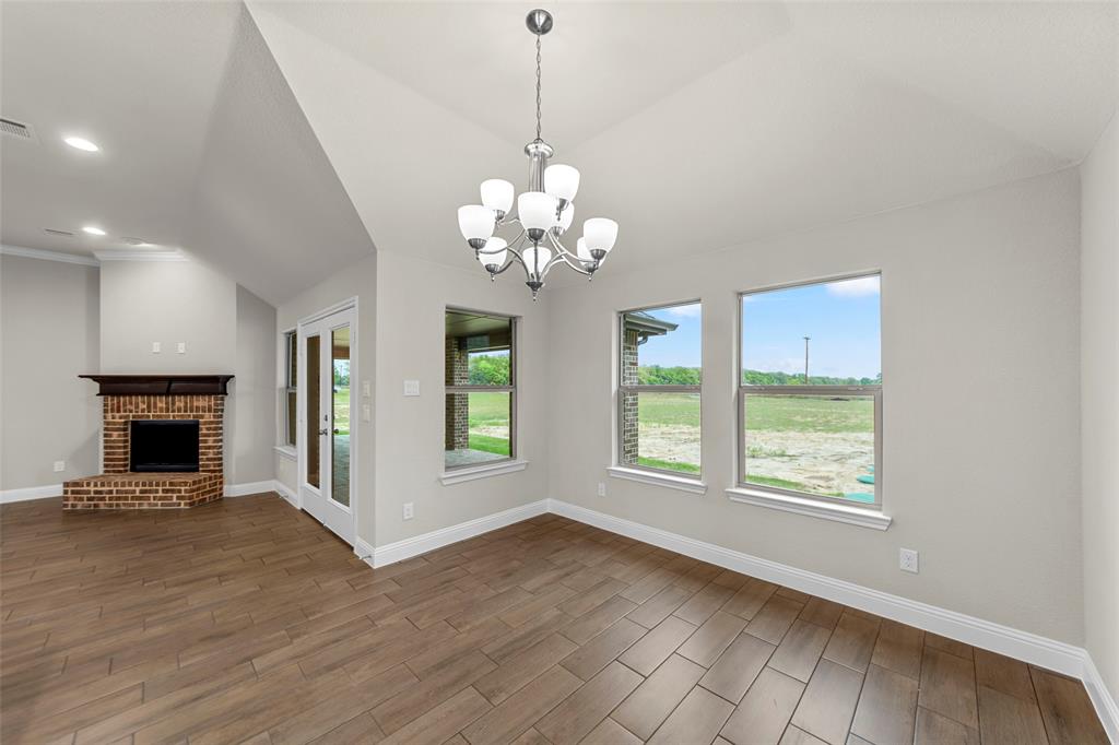 Open concept living space featuring vaulted ceilings, wood-finish flooring, a brick-surround fireplace with a wood mantle, and a glass-paneled door