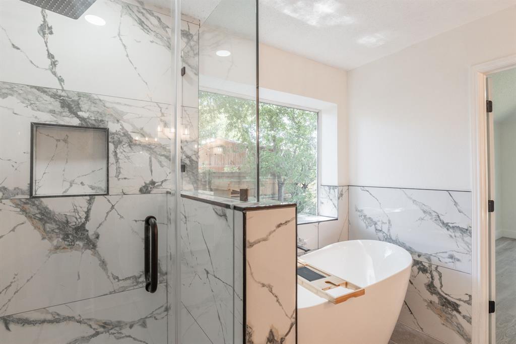 Bathroom featuring a freestanding soaking tub, a walk-in shower with clear glass enclosure and black hardware, and large format marble-look tile