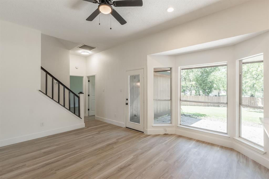 Open-concept living area featuring wood-finish flooring, a contemporary ceiling fan, and a bay window with multiple panes
