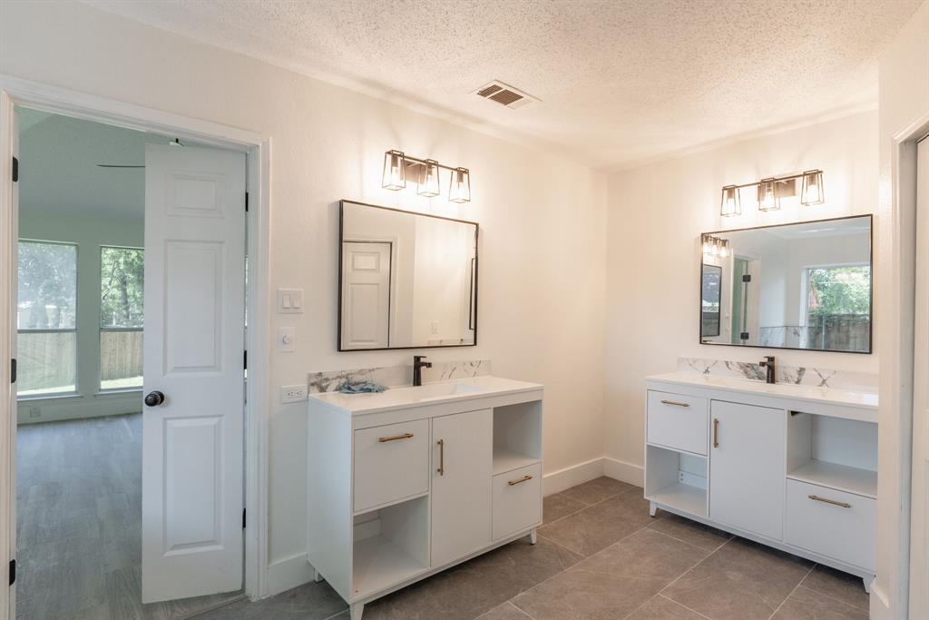 Double vanity bathroom featuring white cabinetry, integrated sinks, dark bronze hardware, and large format floor tiling