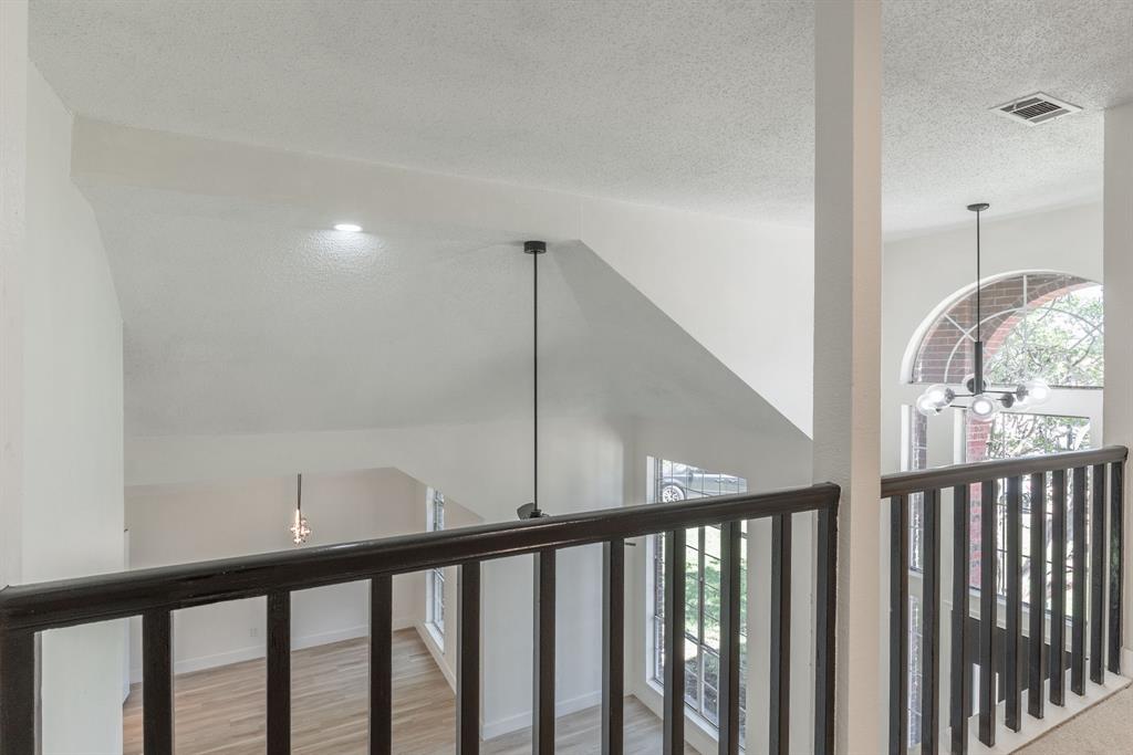 Overlooking space with dark wood railing, arched window, and two distinct pendant light fixtures