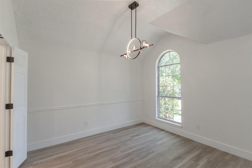 Interior space featuring an arched window, wood-finish flooring, a modern chandelier, vaulted ceiling, and chair rail molding