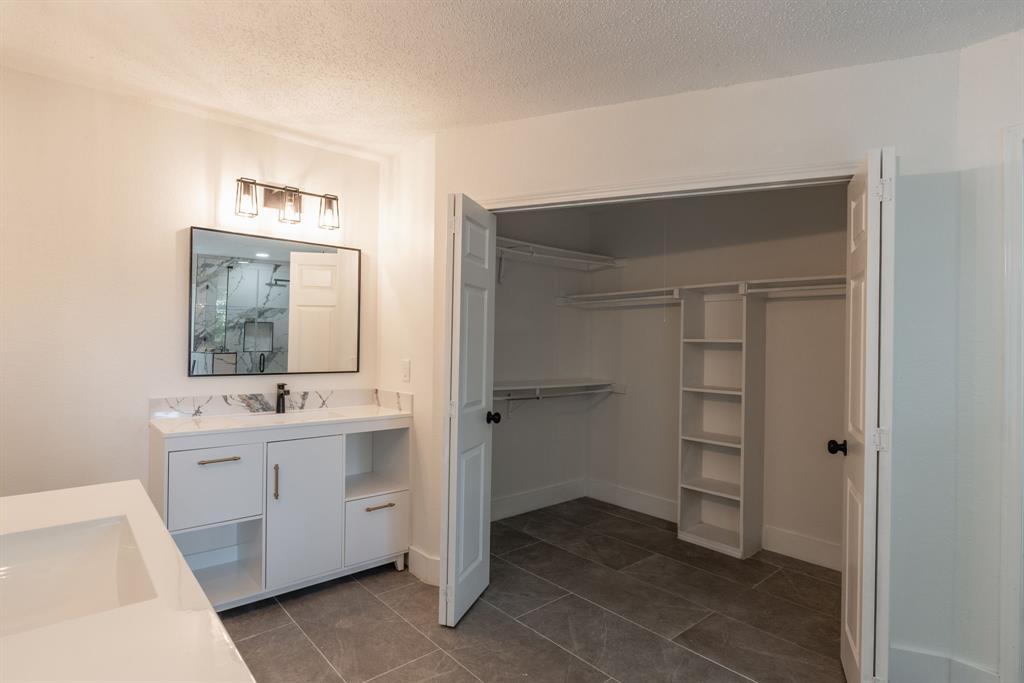Spacious bathroom featuring a dual vanity with white cabinetry, a large mirrored cabinet, and a walk-in closet with built-in shelving
