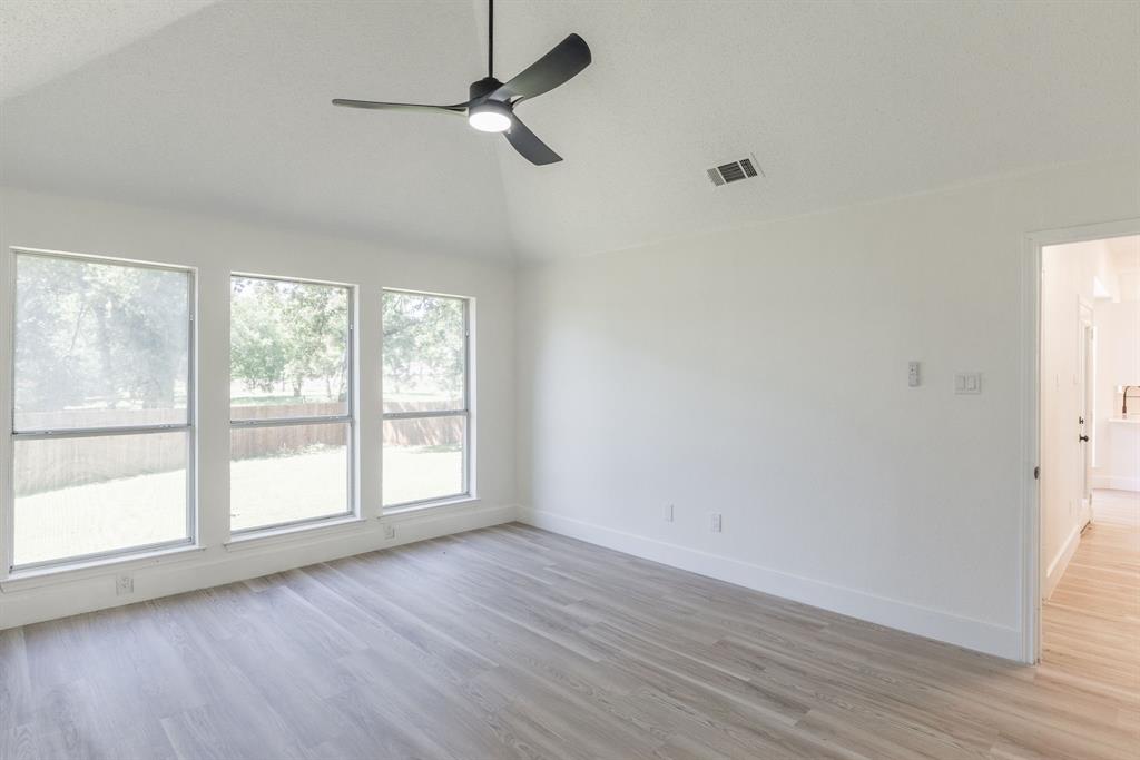 Vaulted ceiling with a contemporary ceiling fan, three large windows overlooking the backyard, wood-finish flooring, and white baseboards