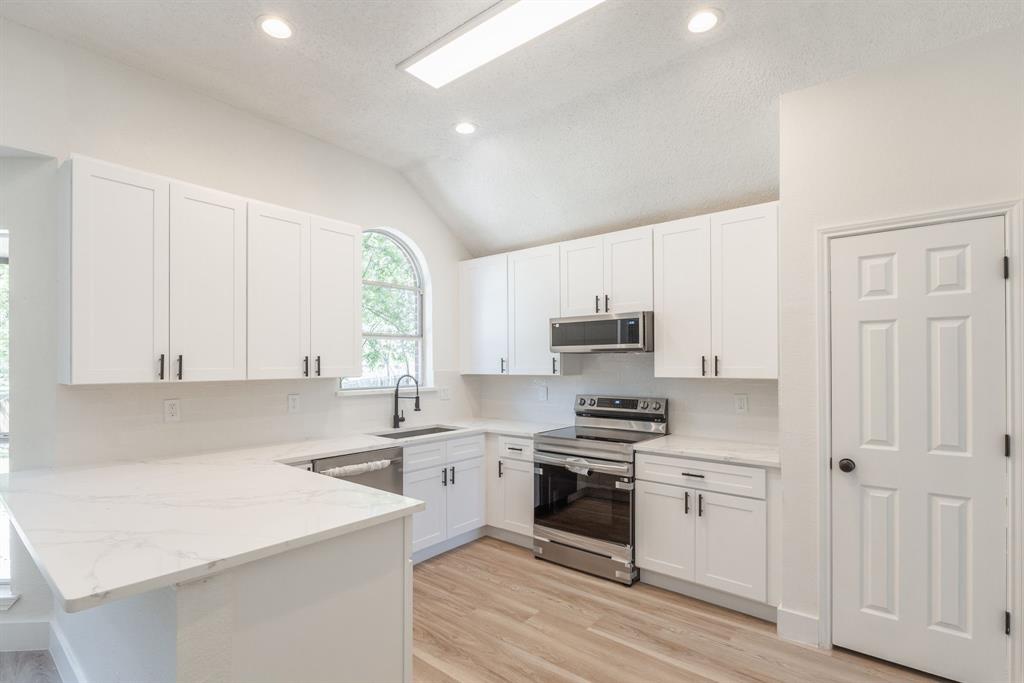 Modern kitchen featuring white shaker cabinetry, stainless steel appliances, marble-look countertops, and wood-finish flooring