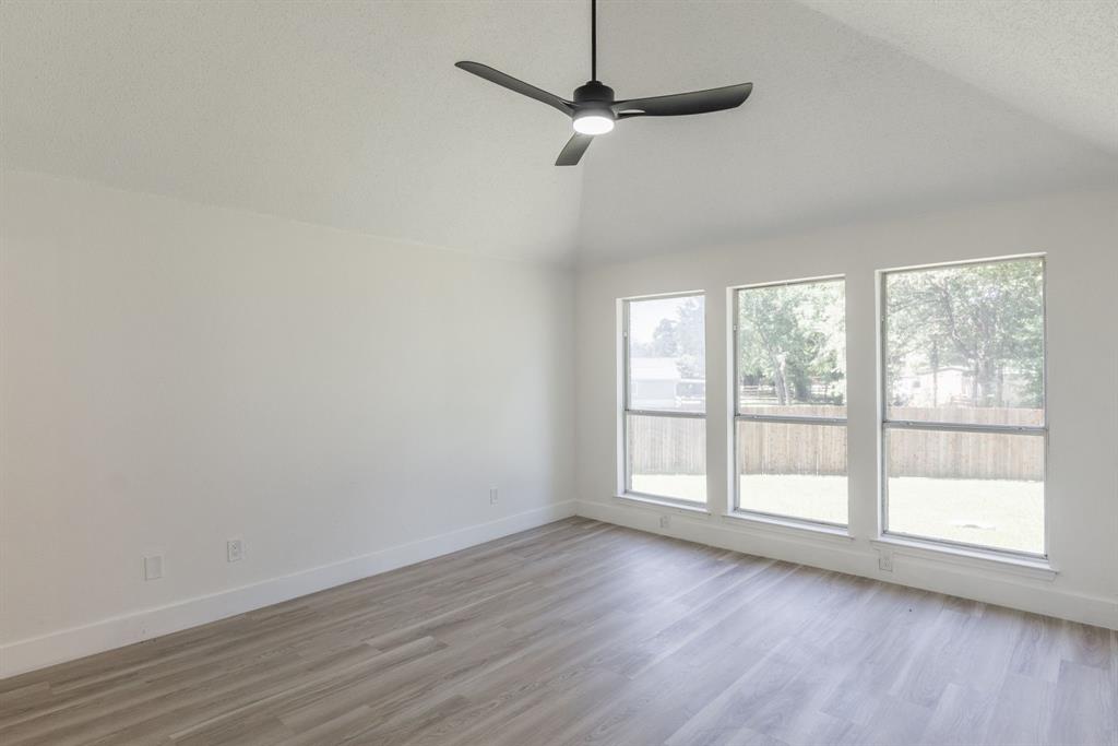 Room with a vaulted ceiling, a modern ceiling fan, three large windows, and light wood-finish flooring