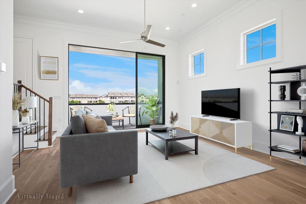 Spacious living area featuring wide plank wood-finish flooring, a contemporary ceiling fan, and large sliding glass doors opening to an outdoor balcony