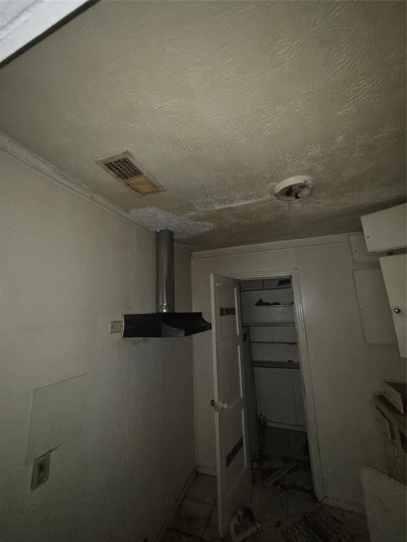 Kitchen area featuring a stainless steel range hood, overhead ceiling vent, and a pantry with shelving