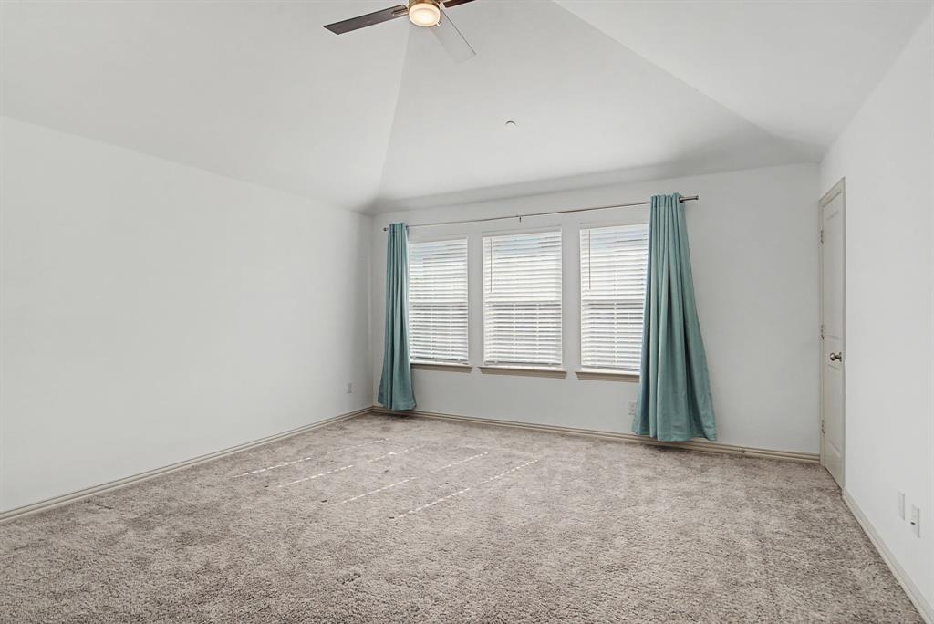 Spacious room featuring vaulted ceilings, plush carpeting, three windows with blinds, and a ceiling fan with integrated lighting