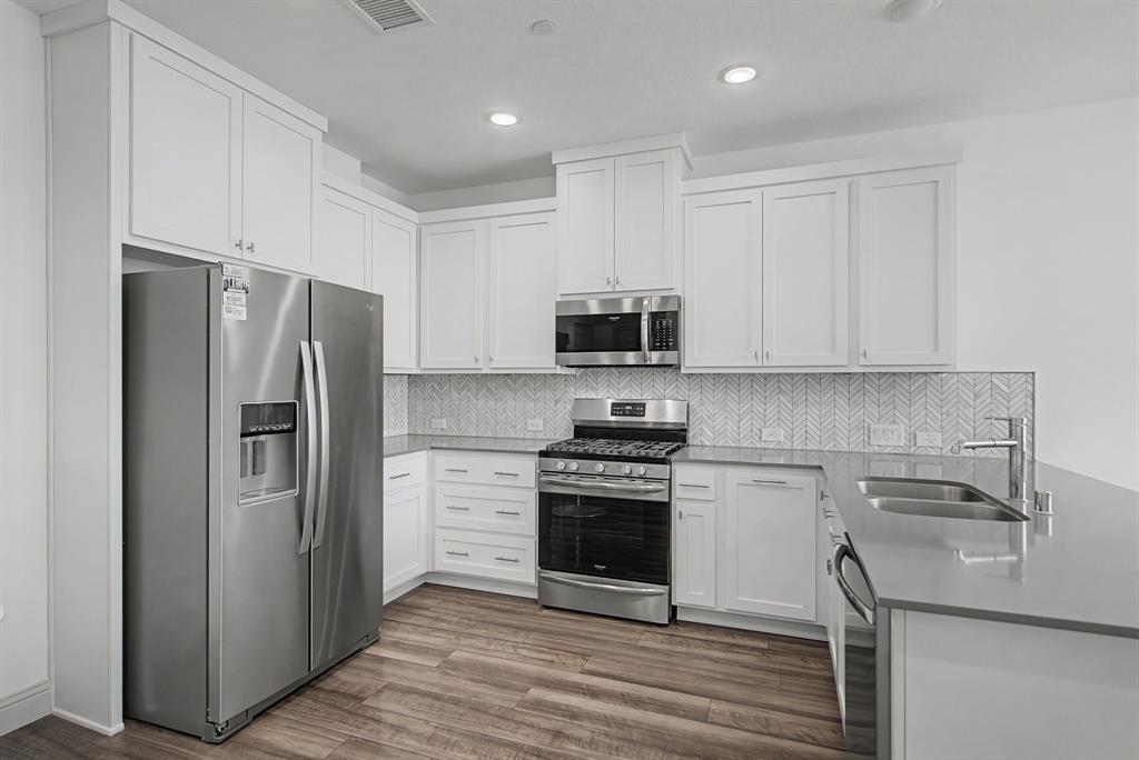 Kitchen featuring stainless steel appliances, white shaker cabinetry, wood-finish flooring, light-toned countertops, and a herringbone tile backsplash