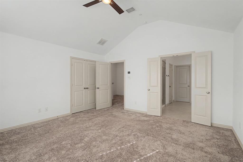 Spacious room featuring vaulted ceilings, light neutral carpeting, and a ceiling fan