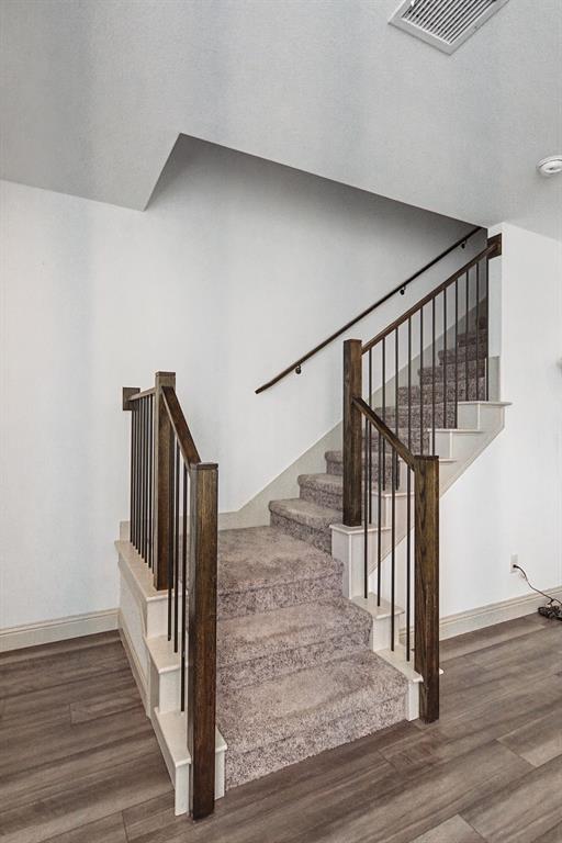 Staircase featuring dark wood newel posts and handrails, black iron balusters, and plush carpeted treads, complemented by wood-finish flooring