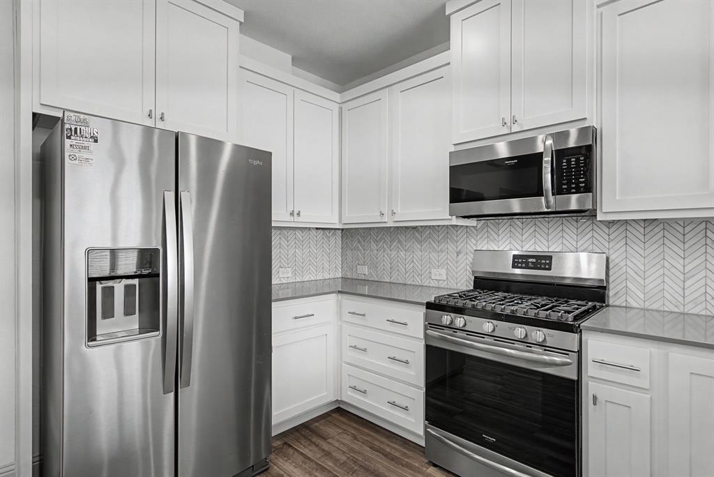 Contemporary kitchen featuring white shaker cabinetry, stainless steel appliances, a herringbone tile backsplash, and wood-finish flooring