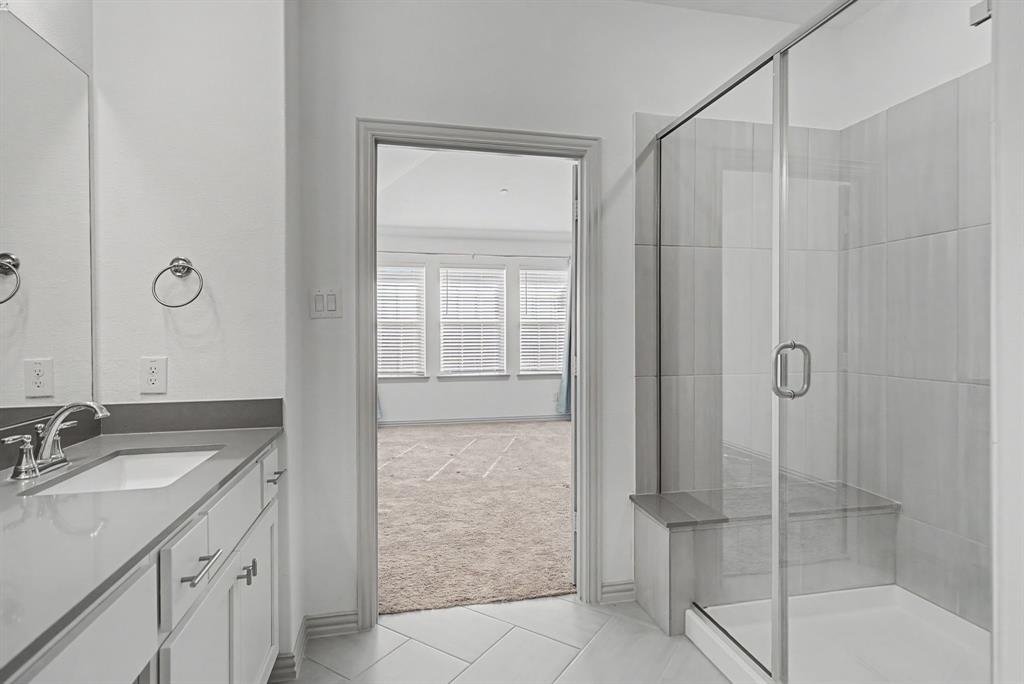 Bathroom featuring a single vanity with an undermount sink, a large wall mirror, and a glass-enclosed shower with a built-in bench