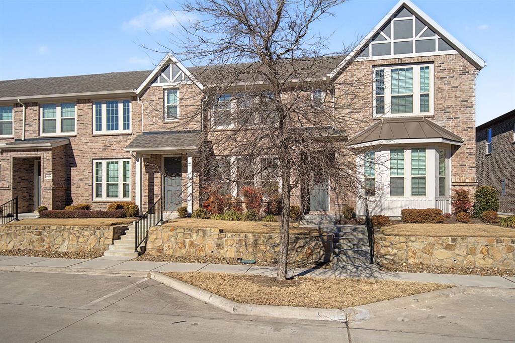 Brick townhome exterior featuring an arched gable detail, bay window, covered entry, black metal railings, and stone retaining walls Brick townhome exterior featuring an arched gable detail, bay window, covered entry, black metal railings, and stone retaining walls