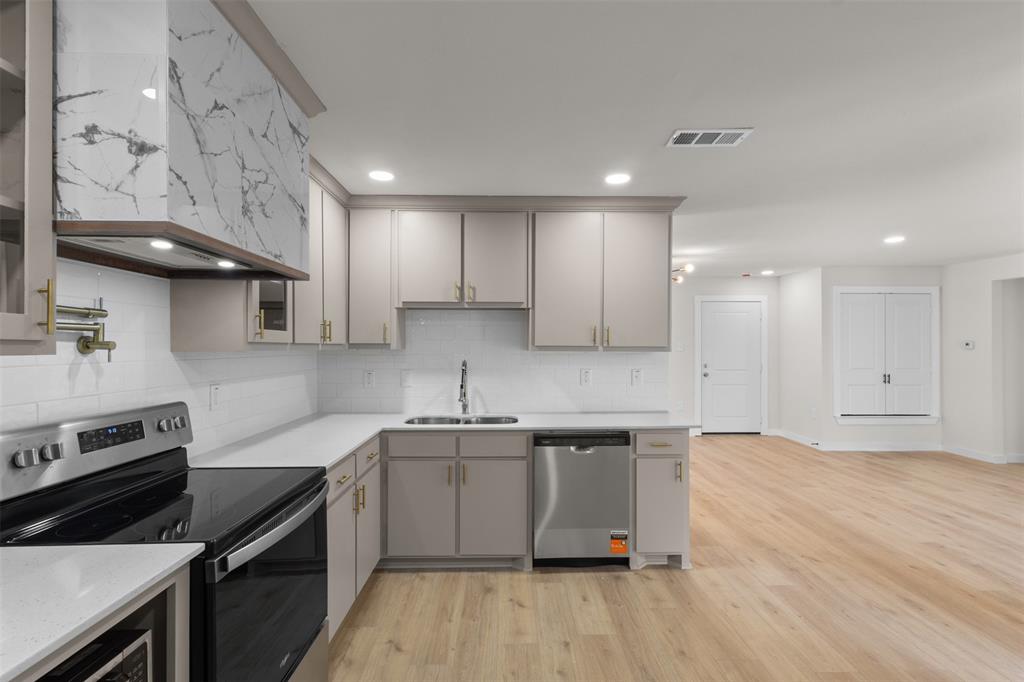 Modern kitchen with light cabinetry, stainless steel appliances, a tile backsplash, and light-toned wood-finish flooring