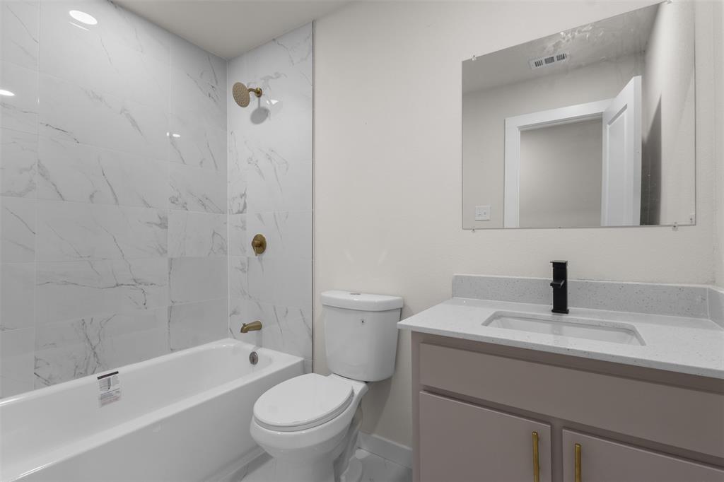 Bathroom featuring a white subway tile surround with brass fixtures, a white bathtub, a toilet, a vanity with a light-toned countertop, and a rectangular mirror