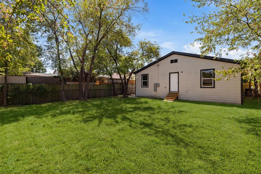 Expansive backyard featuring a lush lawn, mature trees, and a wood privacy fence