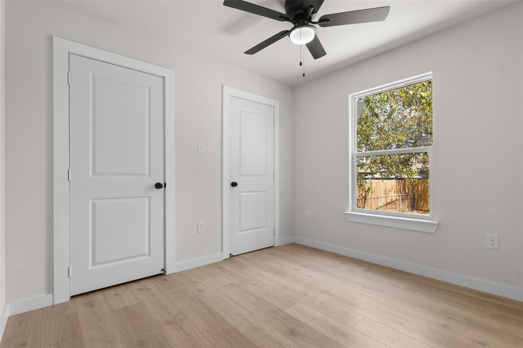 Light-toned wood-finish flooring, white paneled doors with matte black hardware, a window with white trim, and a ceiling fan with integrated lighting