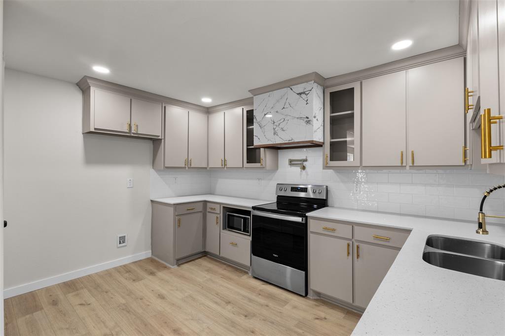 Light-toned cabinetry with gold-toned hardware, white subway tile backsplash, light-toned countertops, stainless steel appliances, and wood-finish flooring