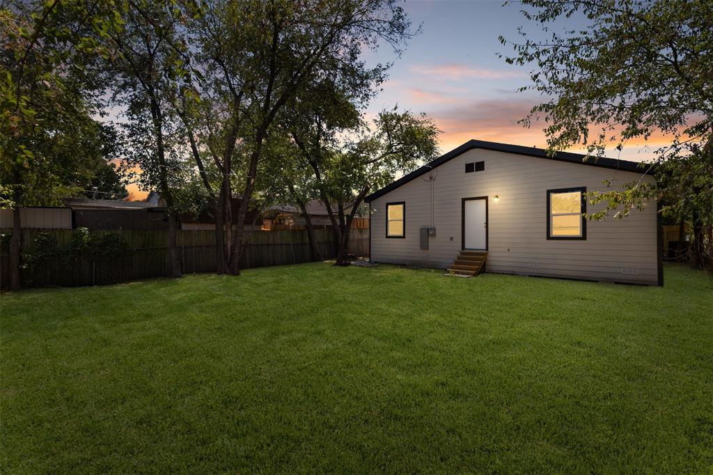 Expansive green lawn with mature trees and a wood privacy fence