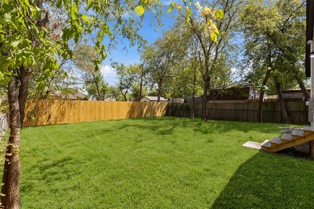 Expansive backyard with a manicured lawn, established trees, and a privacy fence