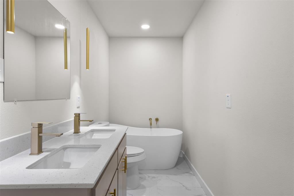 Dual vanity with integrated sinks, freestanding soaking tub, gold-finish fixtures, large wall mirror, and recessed lighting